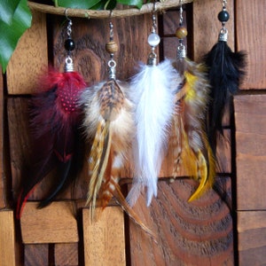 May include: Five pairs of feather earrings with different colored feathers and beads. The earrings are hanging from a wooden surface.