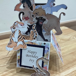 May include: A pop-up card featuring characters from the Jungle Book. The card is open and shows Mowgli, Baloo, Shere Khan, Kaa, and Bagheera. The card has a blue background with a white border and the text "Happy Birthday Ivy".