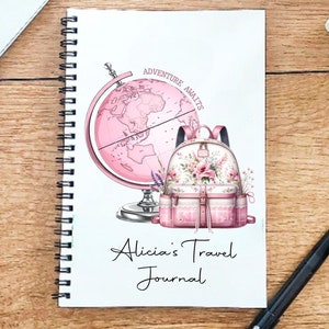 May include: A pink travel journal with a globe and a pink backpack with floral accents. The text on the cover reads "Adventure Awaits" and "Alicia's Travel Journal".