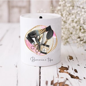 May include: White ceramic money jar with a gold and pink design featuring hair styling tools, including a hairdryer, scissors, and a hair product. The text "Bonnie's Tips" is printed on the jar.