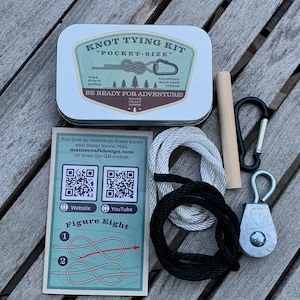 Pode incluir: Um kit de nós de bolso com uma lata de metal, corda, cavilha, roldana, mosquetão e cartão de nós. A lata diz "Knot Tying Kit" e "Be Ready For Adventure!". Um cartão mostra o nó em oito. Códigos QR para site e YouTube.