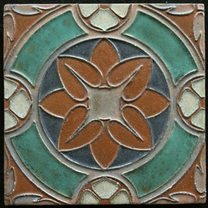May include: A square ceramic tile with a brown, green, and white floral design. The tile has a raised, textured surface.