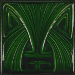 Op de afbeelding: Vierkante groene keramische tegel met een gestileerd Art Nouveau-ontwerp. De tegel heeft een symmetrisch patroon van gebogen lijnen en wervelende vormen in verschillende groentinten, waardoor een gestructureerd, driedimensionaal effect ontstaat. Het ontwerp doet denken aan gestileerde bladeren of stromend water.