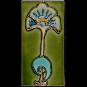 Könnte beinhalten: Rechteckige Keramikfliese mit stilisiertem Blumendesign. Die Blume hat eine hellblaue und gelbe Mitte mit detaillierten Konturen. Der Hintergrund ist strukturiert grün und das Design ist mit einem metallischen Rand umrahmt.