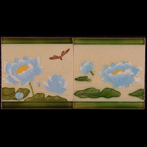 Puede incluir: Dos azulejos de cerámica con fondo crema y borde verde. Los azulejos presentan un diseño de flor de loto azul y amarilla con hojas verdes y una libélula roja.