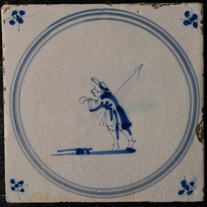 Puede incluir: Azulejo de cerámica blanco cuadrado con una ilustración azul y blanca. La imagen central representa una figura con sombrero y abrigo, sosteniendo un arco y una flecha. Un círculo azul enmarca la imagen central. Diseños florales azules en cada esquina.