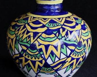 May include: A ceramic vase with a round body and a narrow neck. The vase is decorated with a geometric pattern in shades of blue, yellow, and green.