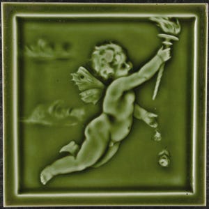 May include: Green ceramic tile with a relief of a cherubic figure holding a torch. The tile is square with a raised border and a matte finish. The cherub has wings and is depicted in mid-flight, with a flower falling from its hand. The tile measures approximately 15 cm x 15 cm.