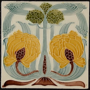 May include: Square ceramic tile with a floral design. The tile features two large yellow flowers with brown centers, surrounded by light blue and green stylized leaves and stems. The background is off-white.