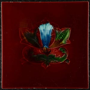 May include: Square ceramic tile with a burgundy background and a central floral design. The flower is blue, with green and red leaves. The tile has a glossy finish and a dark border.