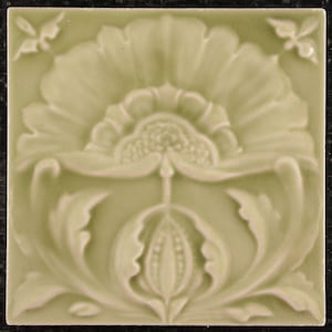 Könnte beinhalten: Eine grüne Keramikfliese mit einem erhabenen Design einer stilisierten Blume mit einer zentralen Knospe und wirbelnden Blättern.