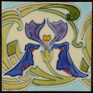 Puede incluir: Azulejo cerámico cuadrado con diseño floral. El azulejo presenta una flor de iris púrpura central con detalles amarillos y naranjas, rodeada de hojas y tallos estilizados verdes y amarillos. El fondo es blanquecino con un borde azul claro.