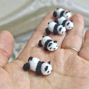 May include: Five small crocheted panda bears in black and white, lying on a hand.