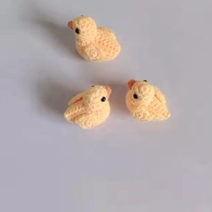 Puede incluir: Tres peque&ntilde;as figuras de pato amarillo de crochet con ojos negros.