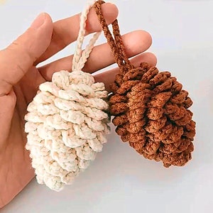 May include: Two crocheted pine cone ornaments, one in white and one in brown, hanging from a string.