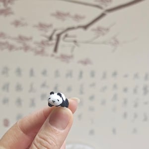 May include: A small crocheted panda bear figurine in black and white, lying on its side with its eyes closed.