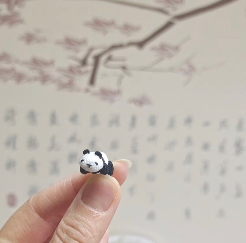 May include: A small crocheted panda bear figurine in black and white, lying on its side with its eyes closed.
