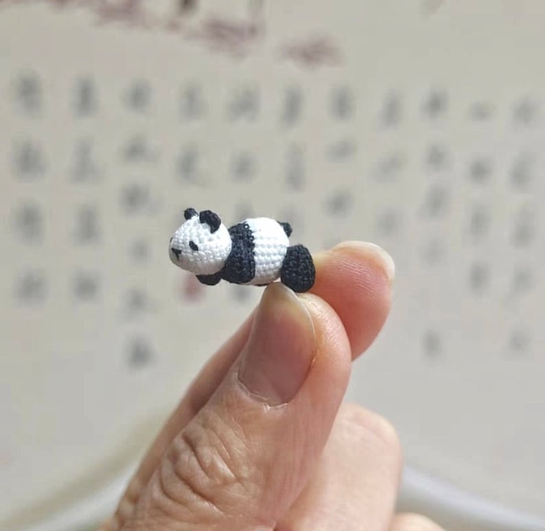 May include: A small crocheted panda bear figurine, lying on its side, with black and white fur.