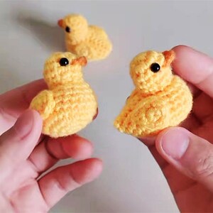 Puede incluir: Tres pollitos amarillos tejidos a crochet con ojos negros. Los pollitos son peque&ntilde;os y tienen una textura esponjosa.