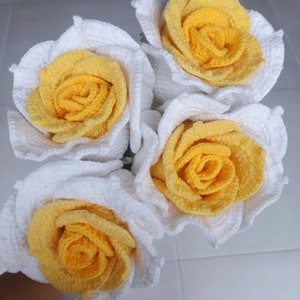 May include: A bouquet of four crocheted roses with white petals and yellow centres.
