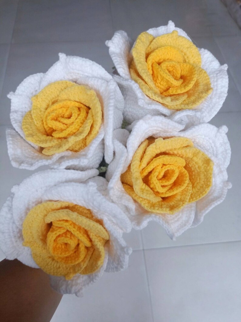 May include: A bouquet of four crocheted roses with white petals and yellow centres.