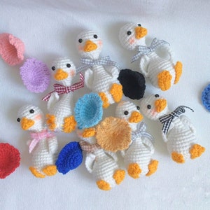May include: A collection of handmade crocheted goose figurines in various colors, including white, yellow, blue, and pink. Each goose has a different hat or accessory, such as a flower, a bow, or a hat.