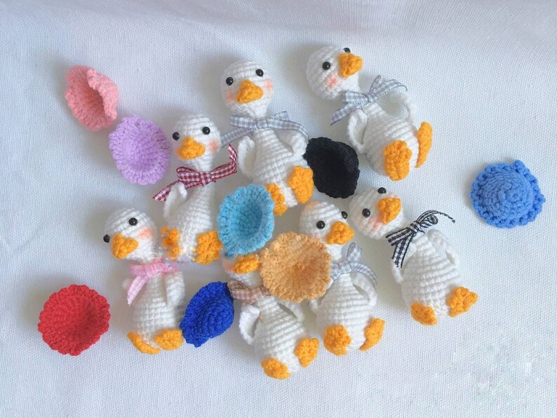 May include: A collection of handmade crocheted goose figurines in various colors, including white, yellow, blue, and pink. Each goose has a different hat or accessory, such as a flower, a bow, or a hat.