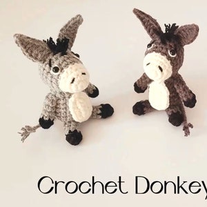 May include: Two crocheted donkey toys, one grey and one brown, sitting on a white surface. The toys have black eyes and noses, and white fur on their bellies. The text "Crochet Donkey" is written below the toys.