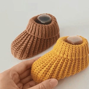 May include: Two pairs of knitted baby booties. One pair is brown and the other pair is yellow.