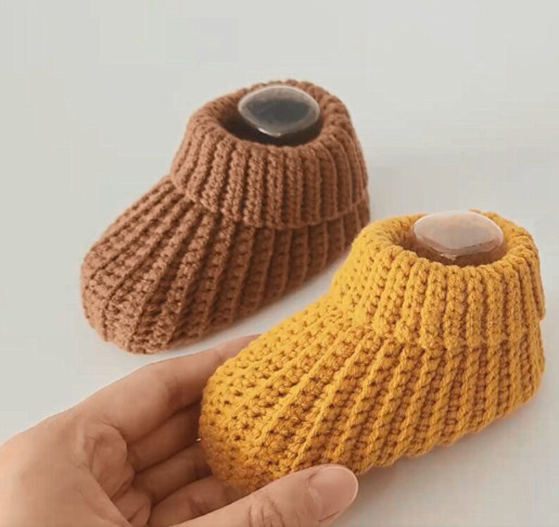 May include: Two pairs of knitted baby booties. One pair is brown and the other pair is yellow.
