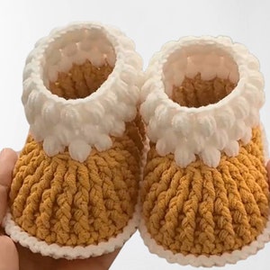 Puede incluir: Un par de botitas de beb&eacute; de crochet en amarillo y blanco. Las botitas tienen un borde de crochet blanco alrededor de la parte superior y un cuerpo de crochet amarillo.