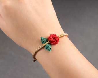 May include: A red rose with green leaves is woven into a gold and brown bracelet.