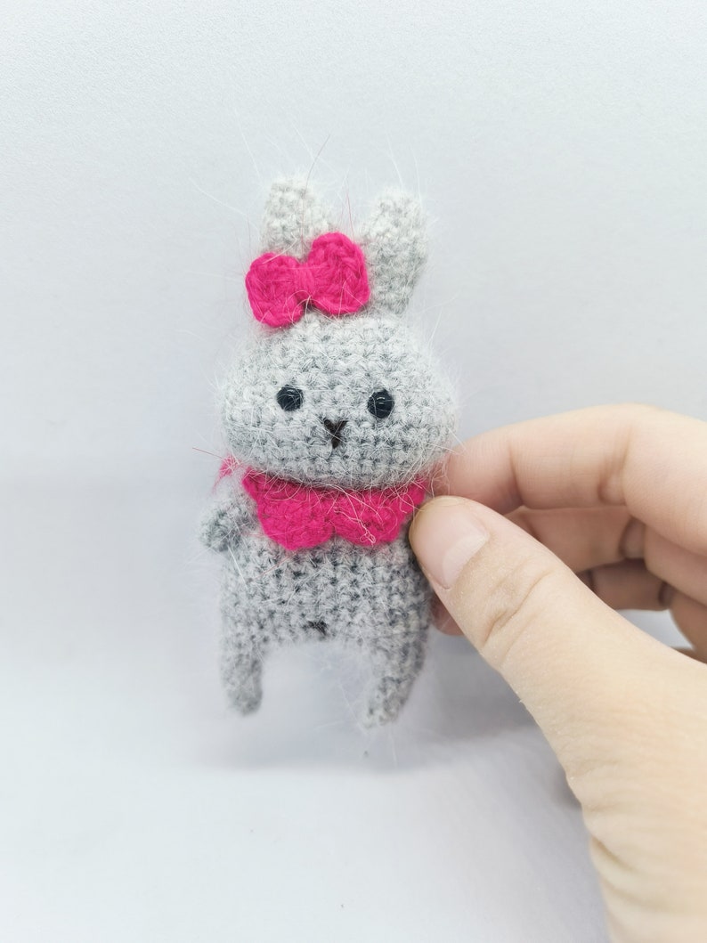 May include: A small gray crocheted bunny with pink ears, a pink bow, and a pink collar.