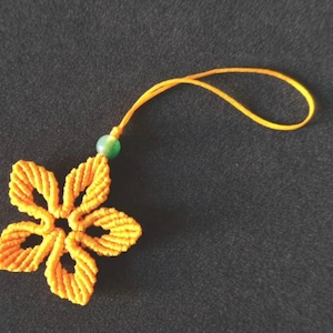 Peut inclure: Un porte-cl&eacute;s en macram&eacute; jaune en forme de fleur avec une perle verte. Le porte-cl&eacute;s est attach&eacute; &agrave; un cordon jaune.