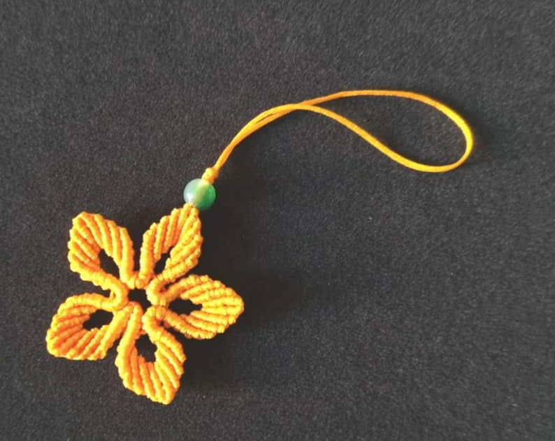 Peut inclure: Un porte-cl&eacute;s en macram&eacute; jaune en forme de fleur avec une perle verte. Le porte-cl&eacute;s est attach&eacute; &agrave; un cordon jaune.