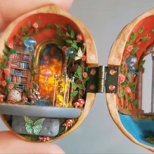 Pode incluir: Um diorama em miniatura dentro de uma casca de noz articulada com uma estante, um portal laranja brilhante, uma gaiola dourada e pequenos cogumelos vermelhos. O interior é decorado com vinhas verdes, rosas cor-de-rosa e uma borboleta verde.
