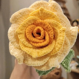 May include: A crocheted rose with a yellow and orange ombre effect. The rose is made with a soft yarn and has a realistic appearance.