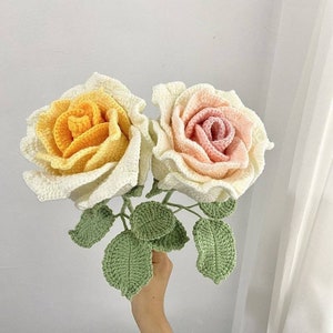 May include: Two crocheted roses, one yellow and one pink, with green crocheted leaves. The roses are arranged in a bouquet.