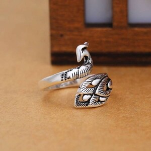 Peut inclure: Bague en argent avec un motif de paon. La bague est r&eacute;glable et s'enroule autour du doigt.