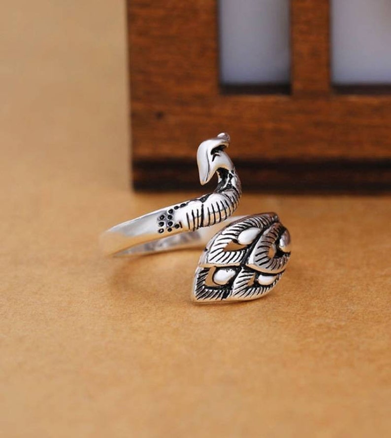 Peut inclure: Bague en argent avec un motif de paon. La bague est r&eacute;glable et s'enroule autour du doigt.
