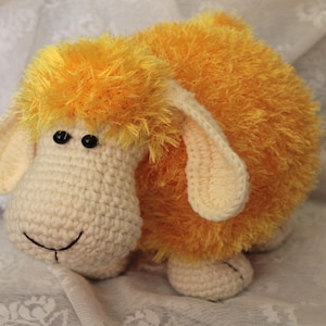 May include: A crocheted stuffed sheep toy with a white body and yellow fluffy fur. The sheep has black eyes and a black nose.