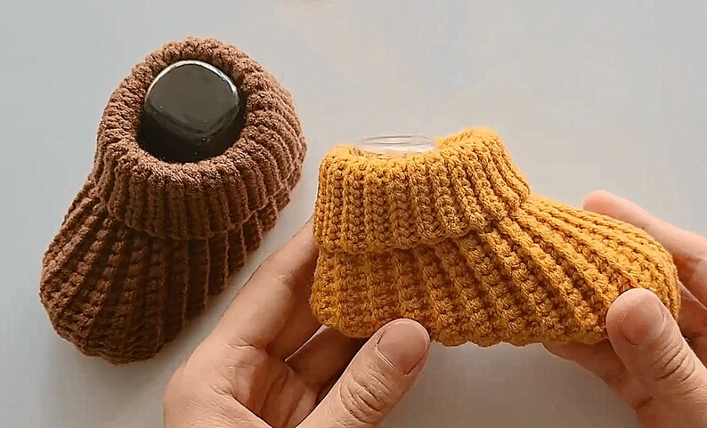 May include: Two pairs of knitted baby booties. One pair is brown and the other pair is yellow.