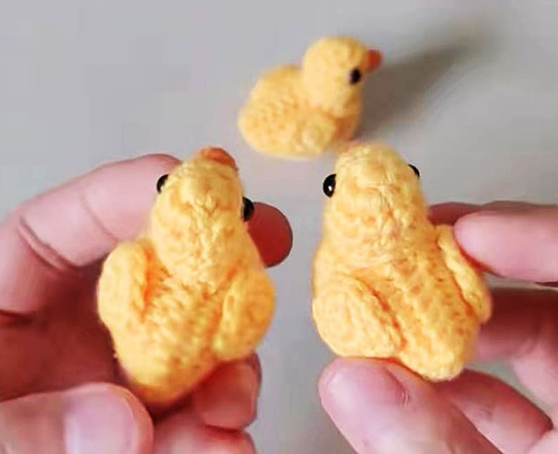 Puede incluir: Tres pollitos amarillos tejidos a crochet con ojos negros. Los pollitos son peque&ntilde;os y tienen una textura esponjosa.
