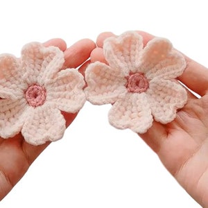 May include: Two crocheted pink flowers with a smaller pink center. The flowers are held in a person's hands.
