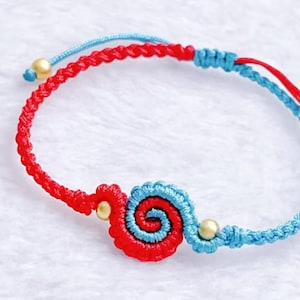 May include: A handmade bracelet featuring a spiral design. The bracelet is crafted with red and blue braided cord, accented with gold-colored beads. The spiral design is a combination of red and blue, creating a visually appealing accessory.