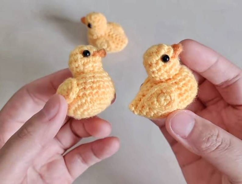 Puede incluir: Tres pollitos amarillos de crochet con ojos negros. Los pollitos son peque&ntilde;os y se sostienen en manos.