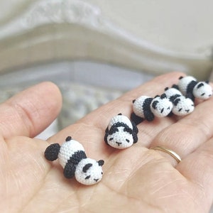 May include: A collection of small crocheted panda bears in black and white, lying on a hand.