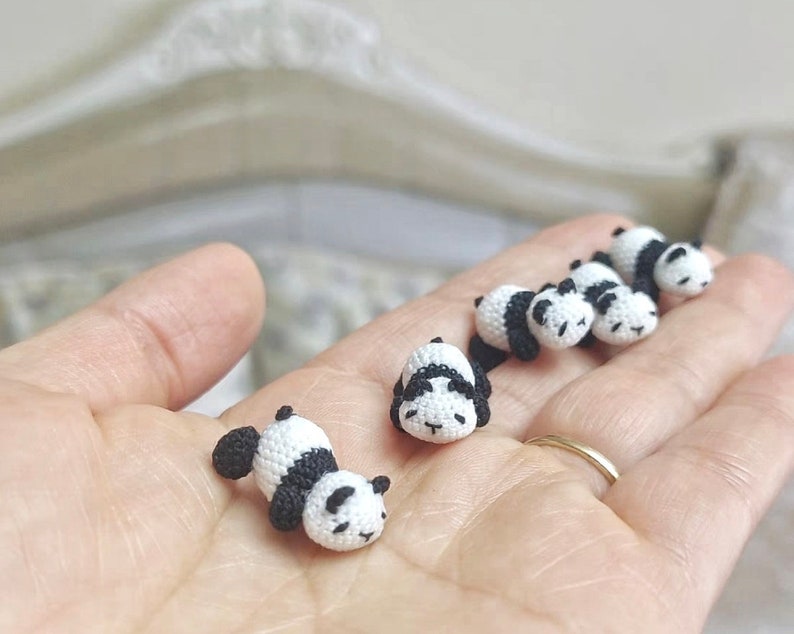 May include: A collection of small crocheted panda bears in black and white, lying on a hand.