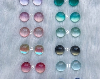 May include: Twelve pairs of 18mm round glass cabochons in various colors, including pink, blue, green, and red. The cabochons are arranged in two rows of six.