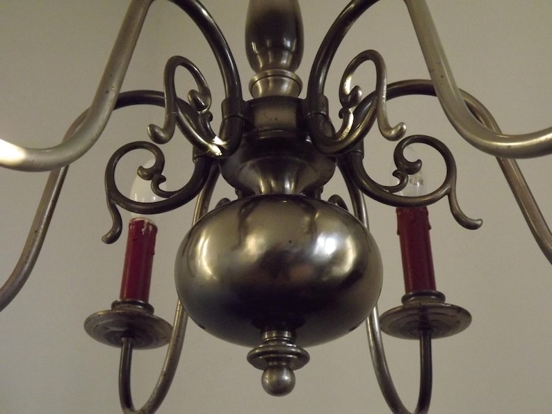 Peut inclure: Un lustre ancien en laiton avec de multiples bras incurv&eacute;s et des volutes d&eacute;coratives. Le lustre comporte des ampoules rouges en forme de bougie et un corps central arrondi. Un luminaire classique.